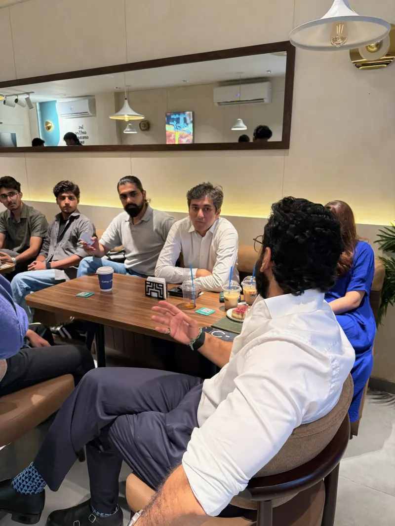 Guests at a long table listening to a man in a white shirt